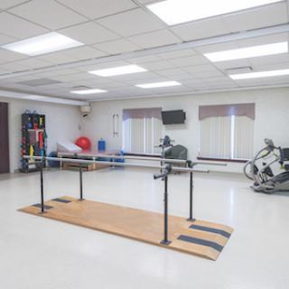 A spacious physical therapy room featuring balance bars and various exercise equipment.