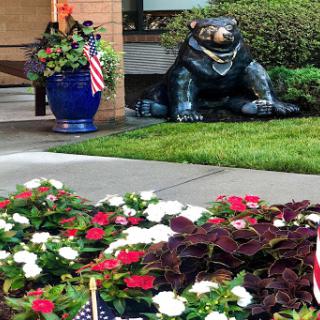A charming garden scene featuring colorful flowers, a bear statue, and decorative planters.