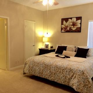 A cozy bedroom with a neatly made bed, decorative pillows, and a floral painting on the wall.