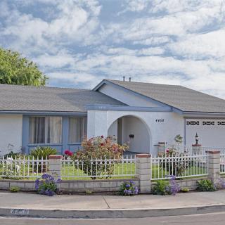 A suburban house with a neatly landscaped front yard and white picket fence under a partly cloudy sky.