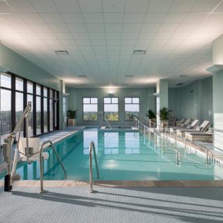 A serene indoor swimming pool with natural light streaming in through large windows, surrounded by comfortable lounge chairs.
