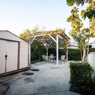 A peaceful backyard with a pergola, patio furniture, and a shed surrounded by trees.