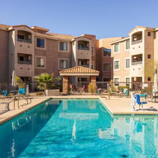 A relaxing residential area featuring a swimming pool surrounded by apartment buildings under a clear blue sky.