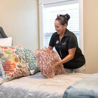 A woman arranging pillows on a bed in a tidy bedroom.