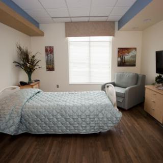 A cozy and well-lit bedroom featuring a neatly made bed, comfortable chair, and decorative elements.