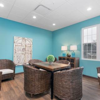 A cozy seating area with wicker chairs and a wooden table, accented by a blue wall and decorative artwork.