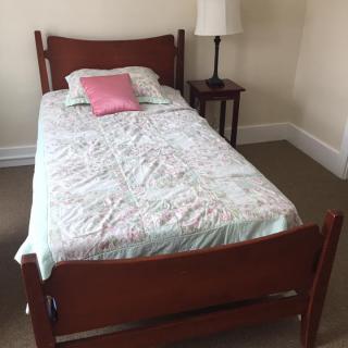 A single bed with a floral bedspread and pink pillow next to a nightstand and lamp.