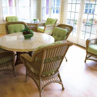 A sunlit dining area with wicker chairs featuring green cushions and a round table.