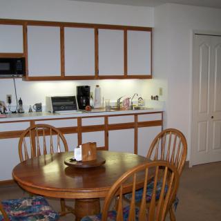 A kitchen and dining area featuring a wooden table with chairs, cabinets, and various appliances.