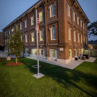 A historic brick building with a well-maintained lawn and flagpole during the evening.