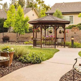 A beautifully landscaped garden featuring a wooden gazebo and a winding concrete pathway.