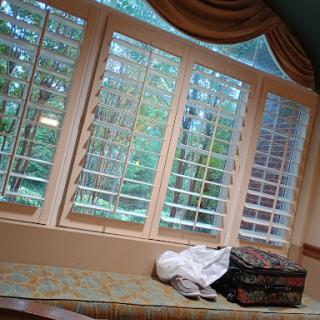 A cozy sitting area featuring large windows with wooden blinds, letting in natural light and a view of the greenery outside.