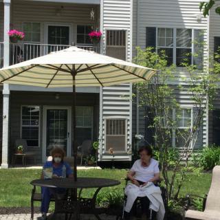 Two people sitting outside under an umbrella in a garden area of an apartment complex.