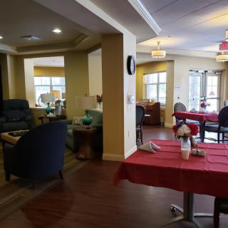 A cozy lounge and dining area with tables and chairs, featuring natural lighting from large windows.