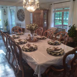 An elegantly set dining room with a large table, surrounded by chairs and adorned with a chandelier.