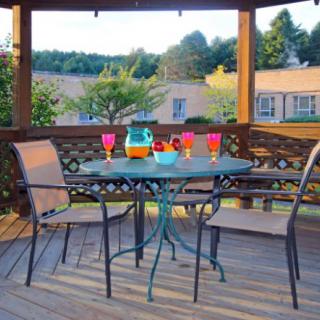 A cozy outdoor patio setup with a table and chairs, featuring colorful glasses under a wooden pergola.