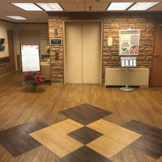 A lobby area featuring an elevator with decorative wooden flooring and various signs.