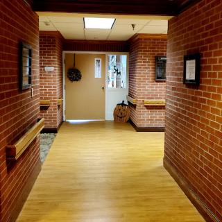 A well-lit corridor featuring brick walls and wooden flooring, adorned with artwork.
