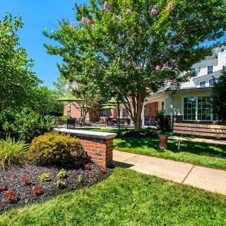 A well-maintained garden with a brick wall, trees, and a pathway leading to the house.