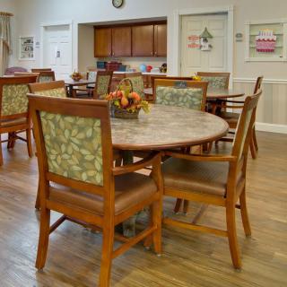 A cozy dining area featuring wooden tables and chairs with floral upholstery, set on a polished wooden floor.