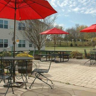 A sunny patio with red umbrellas, tables, and chairs outside a building.