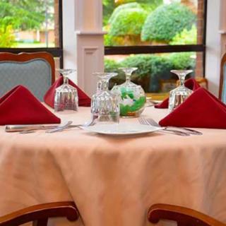 A beautifully set dining table with red napkins and elegant glassware near a window overlooking a garden.