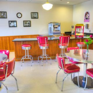 A retro diner with red chairs and bar stools, featuring vintage decor and a popcorn machine.