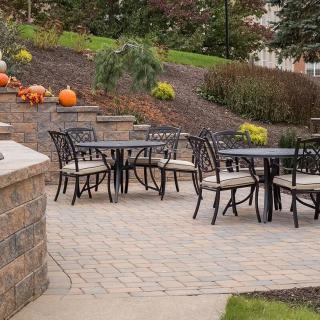 An outdoor patio area with tables and chairs, decorated with pumpkins and surrounded by landscaped greenery.