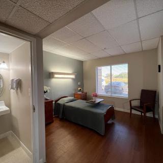 A well-lit hospital room featuring a bed, private bathroom, and seating area.