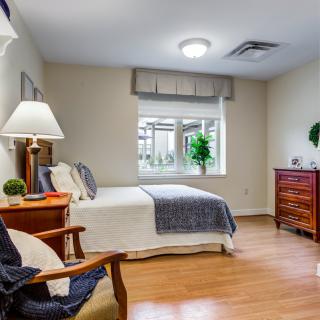 A cozy and minimalist bedroom with modern furnishings, featuring a wooden floor and large window providing ample natural light.