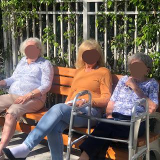 Three women sitting on a bench outdoors in the sunshine.