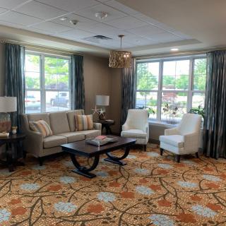 A cozy living room with a sofa, armchairs, and a coffee table, featuring large windows and decorative elements.