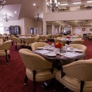 An elegantly set dining area with round tables and comfortable chairs, adorned with chandeliers overhead.