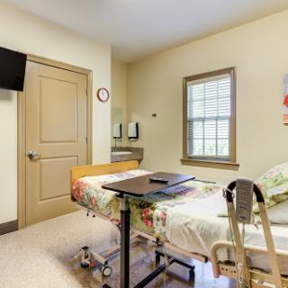 A well-lit patient room in a hospital featuring a bed, television, and window.