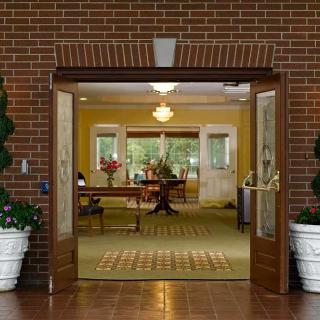 A welcoming entrance with a view of an elegant interior, featuring a brick facade, wooden double doors, potted plants, and stylish furniture.