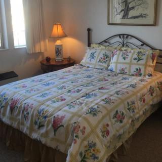 A cozy bedroom with a neatly made bed featuring a floral quilt and matching pillows, illuminated by a bedside lamp.
