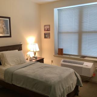 A cozy bedroom with a single bed, lamp, and window.