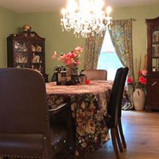 A traditional dining room with a chandelier, table with floral cover, and elegant decor.