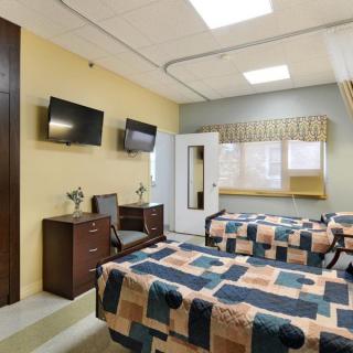 A hospital room with two beds and televisions on the wall.