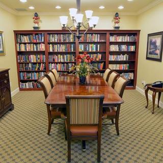 A formal library room with a central table surrounded by chairs and flanked by bookshelves.