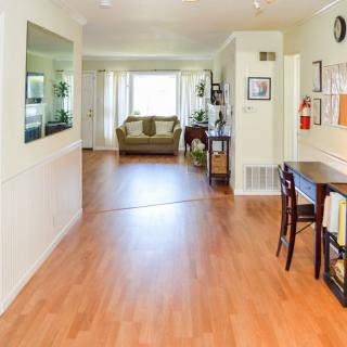 A bright and inviting interior with a hardwood floor, leading from the hallway to a cozy living room area.