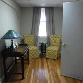 A small office space with two chairs, a desk, and a lamp near a window.