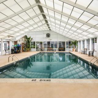 Spacious indoor swimming pool with a glass roof, surrounded by seating and plants.