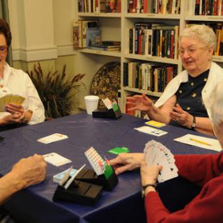 A group of elderly friends enjoying a lively card game together in a cozy library setting.