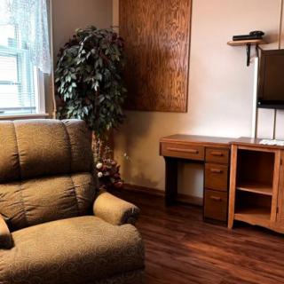 A cozy living room corner with an armchair, desk, and TV.