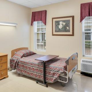 A well-lit hospital room featuring a bed, bedside table, and windows with curtains.