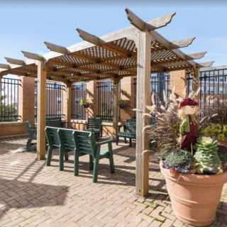 A sunny patio featuring a wooden pergola with green chairs and large planters.