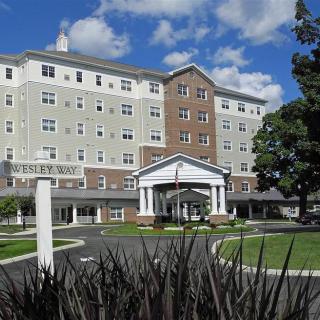 A multi-story residential building with a landscaped entrance under a blue sky with clouds.