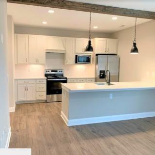 A modern kitchen with white cabinets and stainless steel appliances, featuring an open floor plan and pendant lighting.