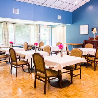 A cozy dining area with tables set for meals, adorned with flowers and bathed in natural light.
